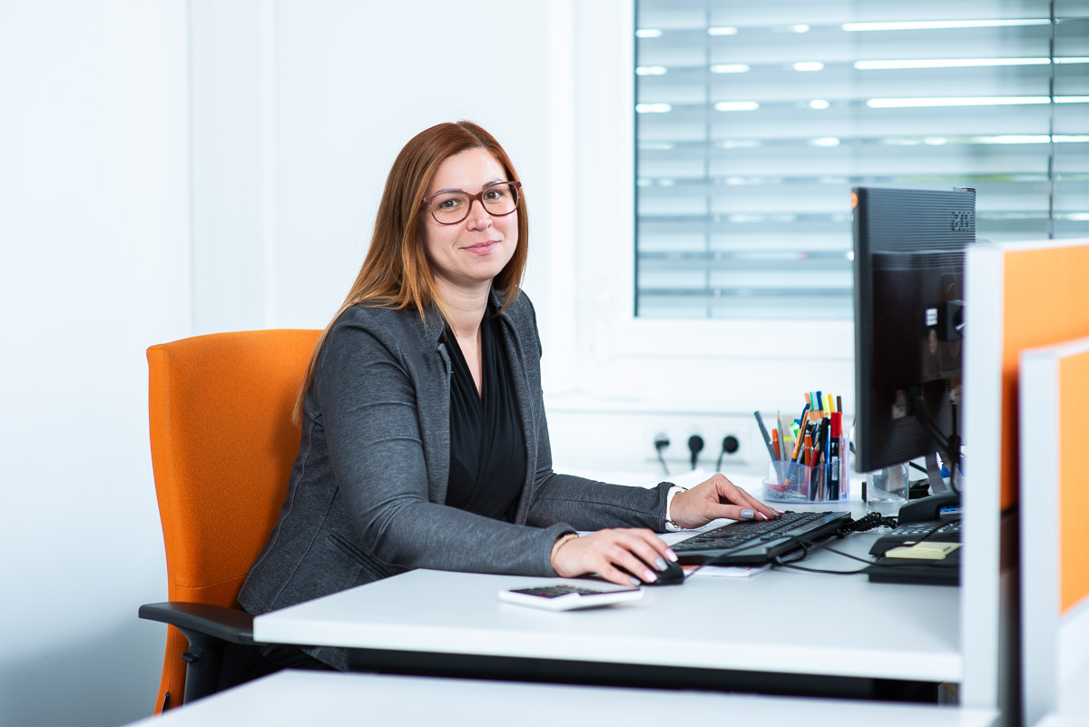 Business Fotografie mit einer lächelnden Frau, die am Schreibtisch vor einem Monitor sitzt. Unternehmensfotografie für den Dachspezialisten Bauder