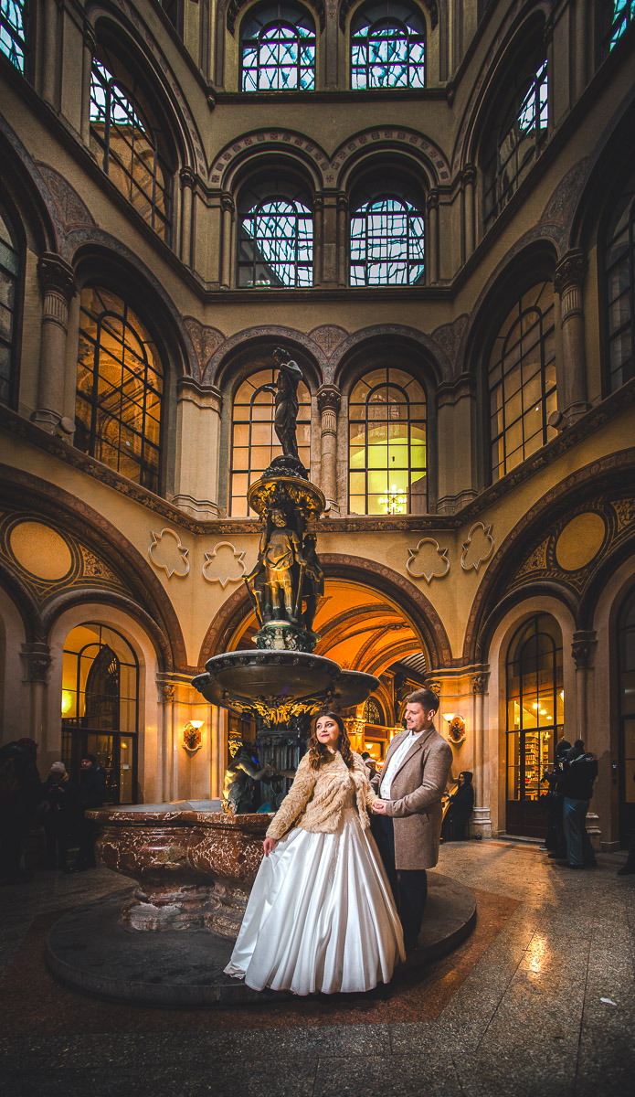 Ein Brautpaar lächelt glücklich und posiert einem Brunnen in der Ferstel Passage Wien. Romantische Hochzeitsfotografie