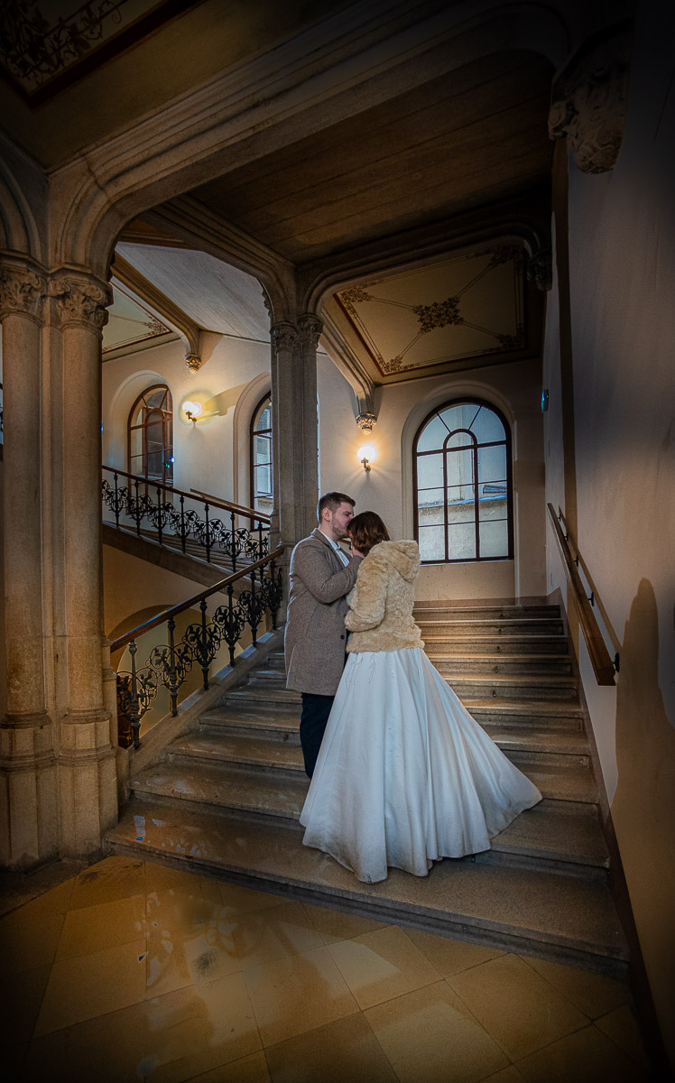Ein glückliches Brautpaar steht und küsst sich auf den Treppen eines Gebäudes. Romantische Hochzeitsfotografie