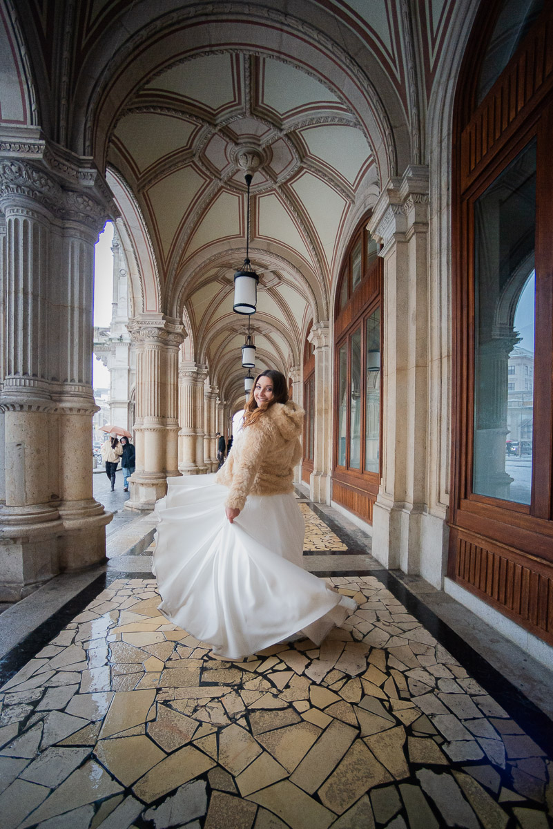 Eine lächelnde Braut tanzt, dreht sich fröhlich und posiert für ein Foto unter den Arkaden der Wiener Staatsoper.