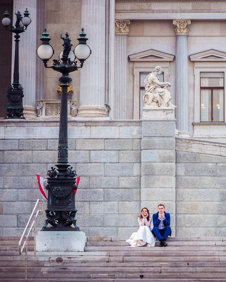 After-Wedding-Hochzeitsfoto von Braut und Bräutigam auf den Treppen des Österreichischen Parlaments in Wien, lachend in einer humorvollen Pose vor der beeindruckenden Architektur, aufgenommen von Fotograf Alexandru Bialis aus Österreich