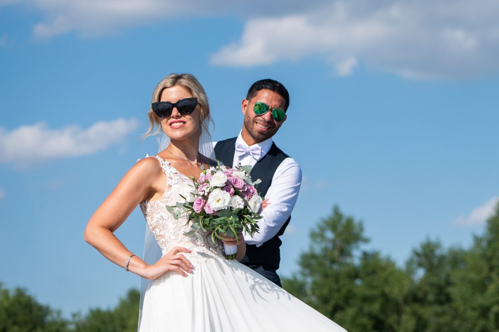 Brautpaar mit Sonnenbrille und Brautstrauß vor blauem Himmel – Hochzeitsfotografie im Burgenland