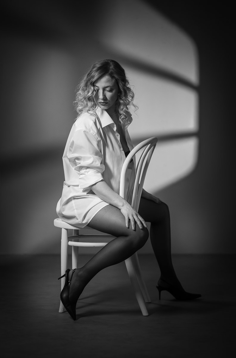 Sinnlichkeit und Licht – vertikales Schwarzweiß-Frauenporträt im Fotostudio mit sitzender Pose